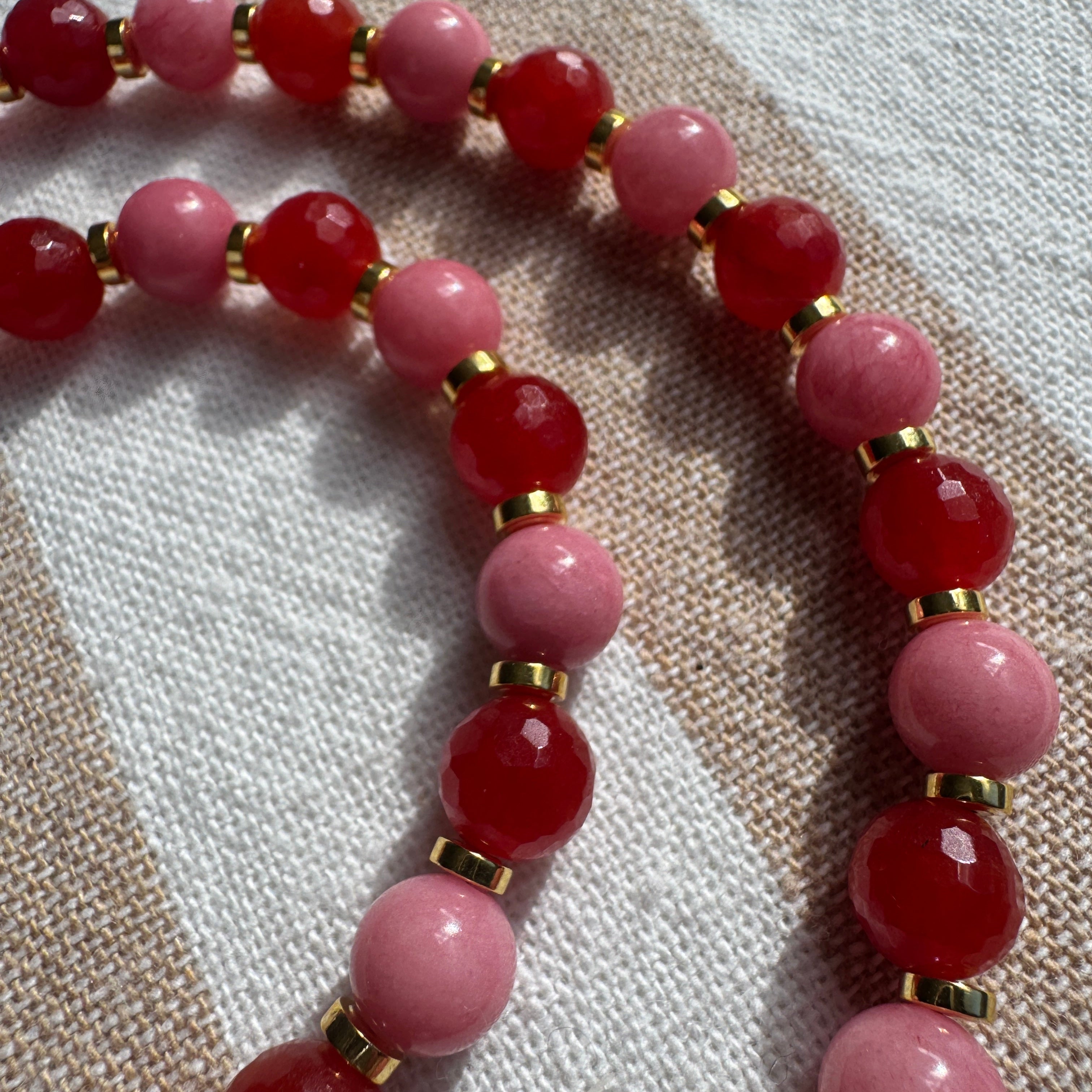 Beaded necklace with pink and red beads on a textured fabric background