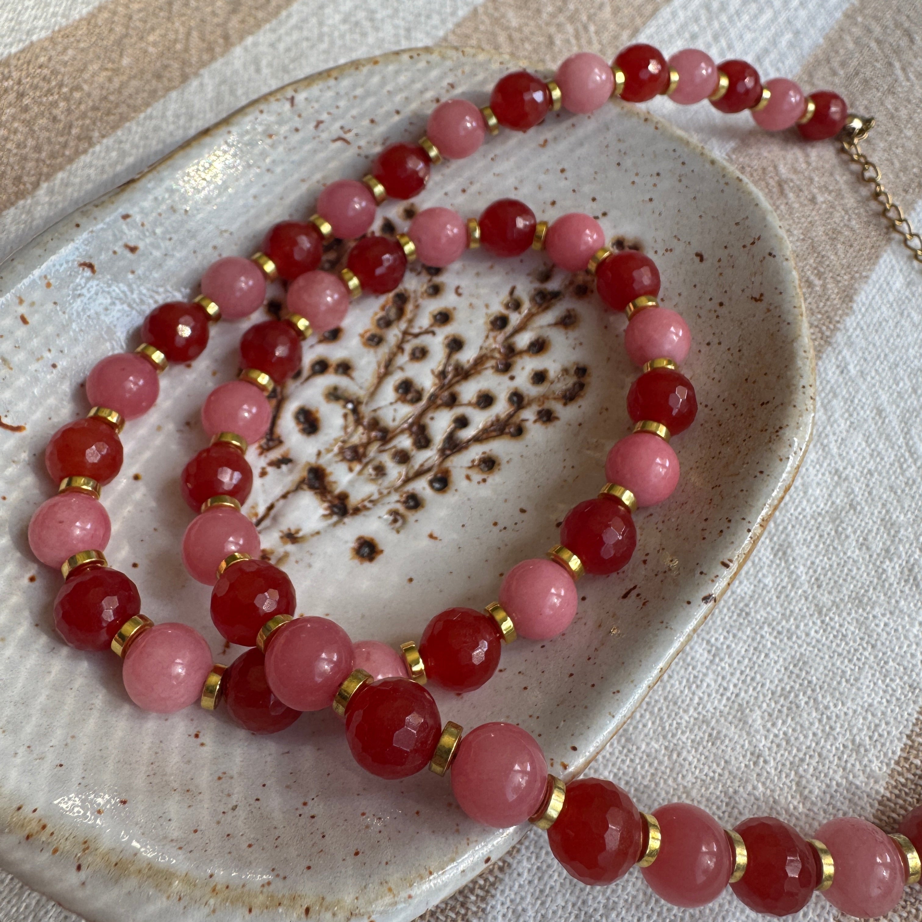 Beaded necklace with pink and red beads on a ceramic dish