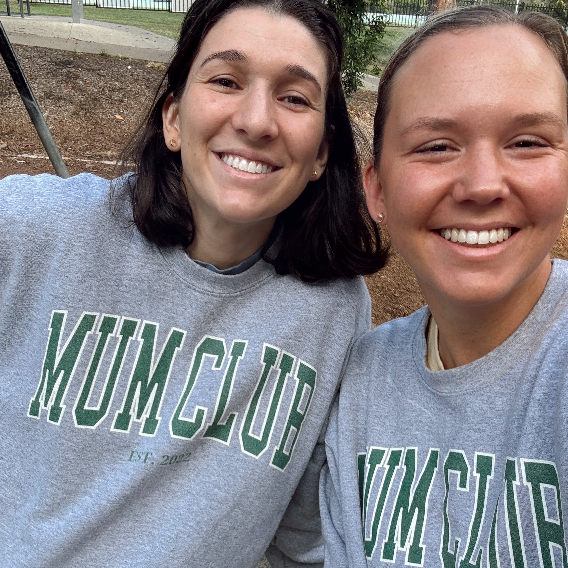 Two people wearing gray sweatshirts with green text, standing outdoors.