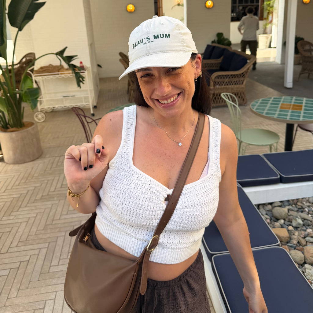 Woman wearing a white cap and top, holding a phone, in an outdoor setting.