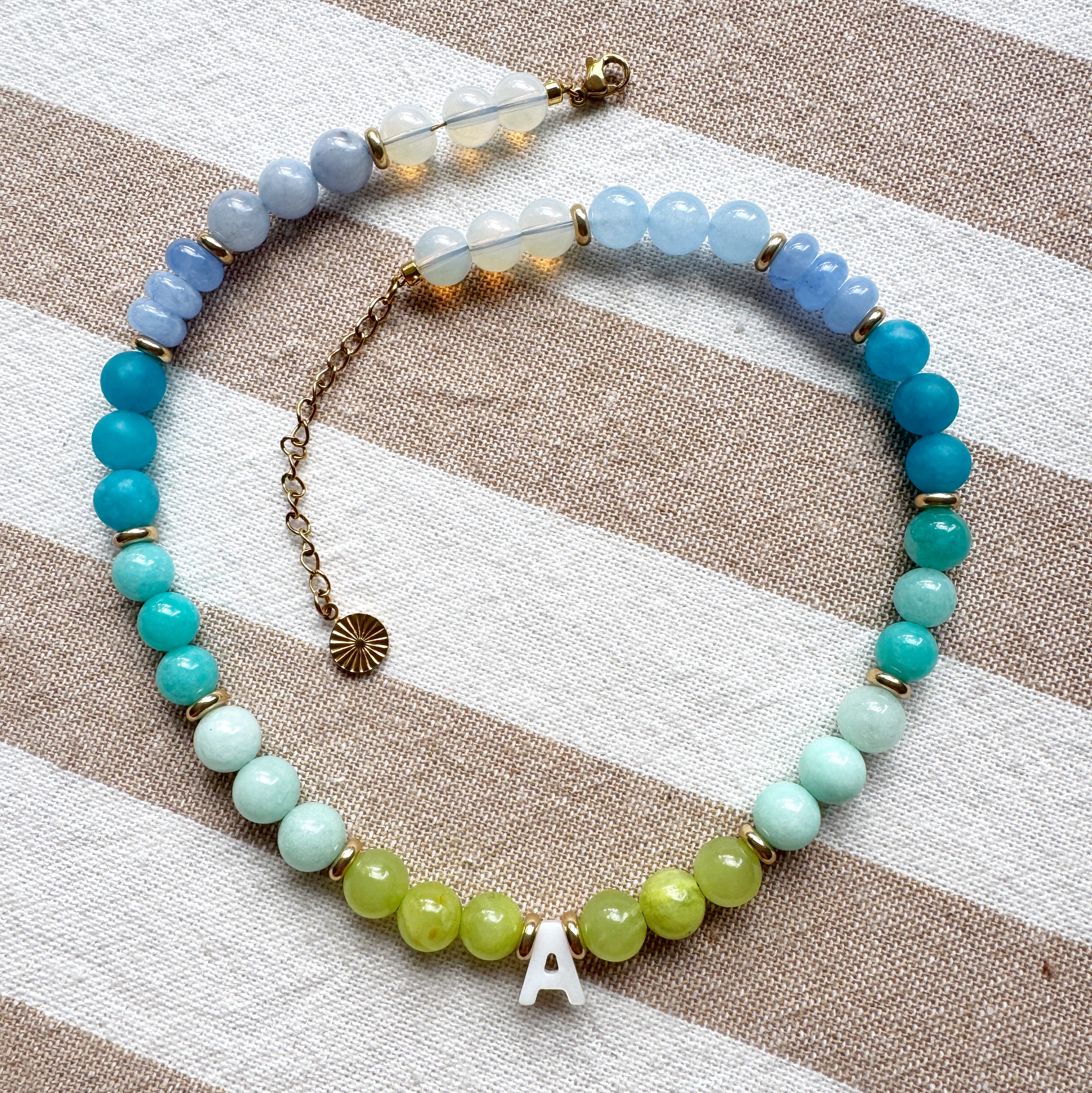 Necklace with blue, green, and gold beads on a striped fabric background