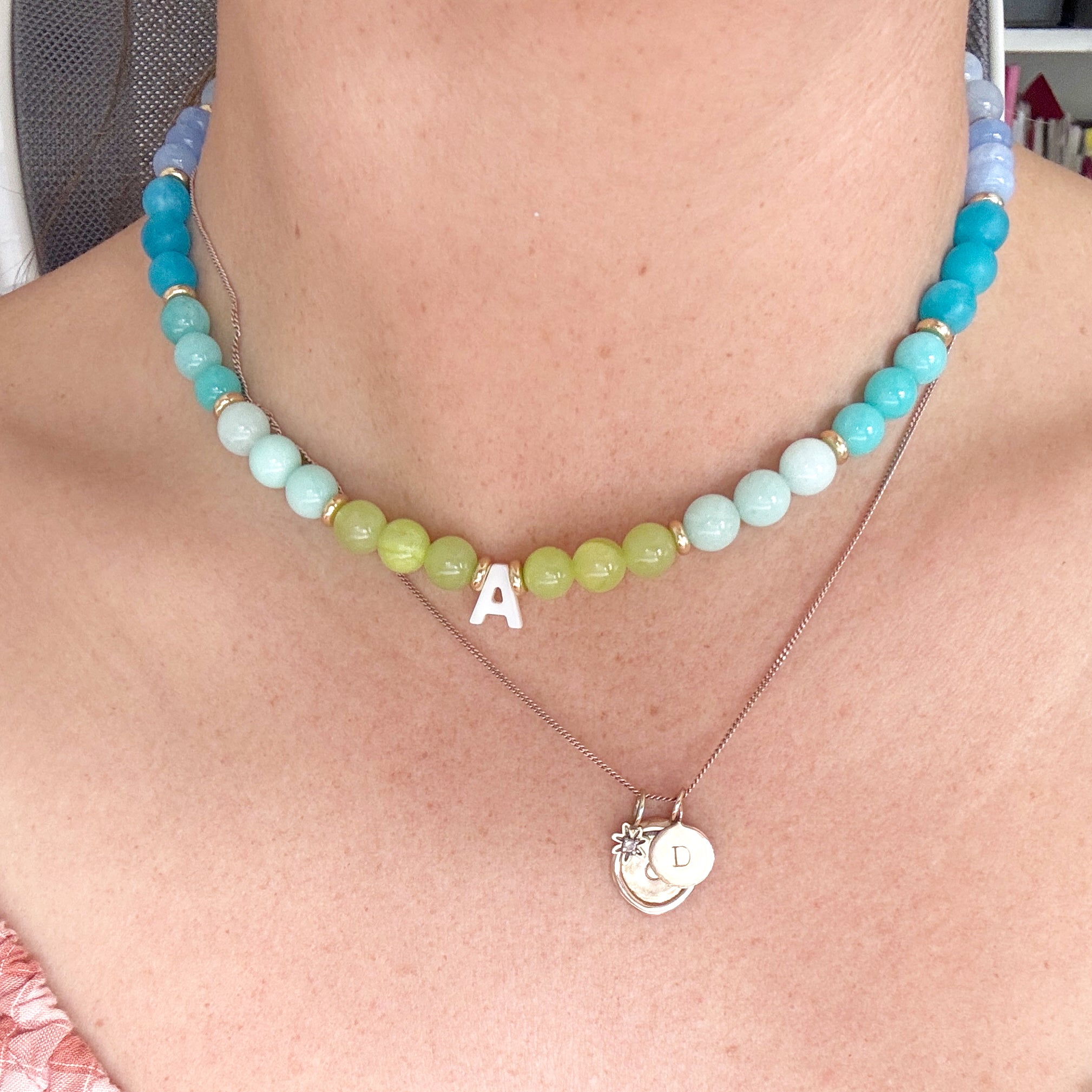 Necklace with blue and green beads and a letter 'A' pendant on a person's neck.