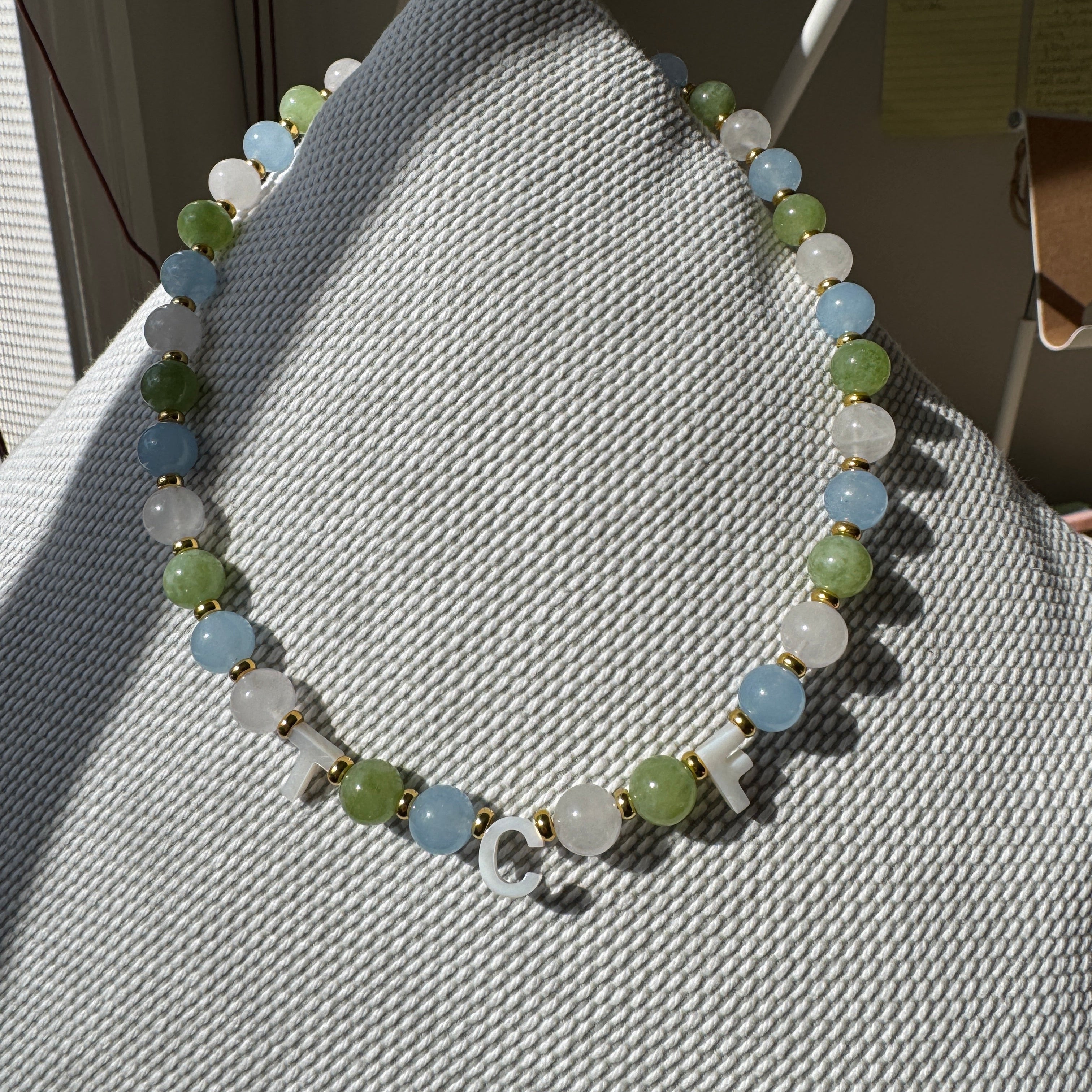 Beaded bracelet with green and white stones on a textured surface