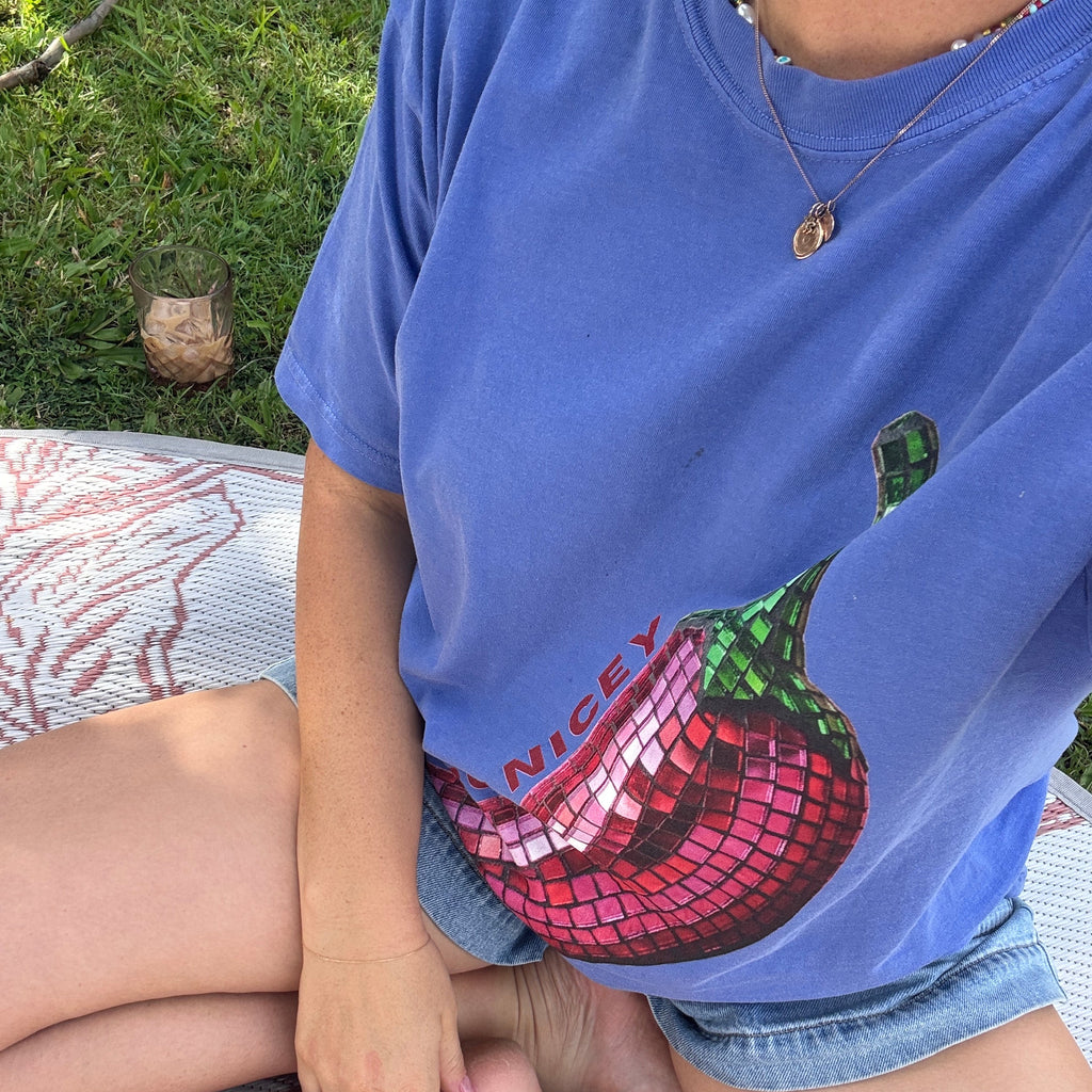 Person wearing a blue shirt with a colorful design sitting on a patterned blanket outdoors.