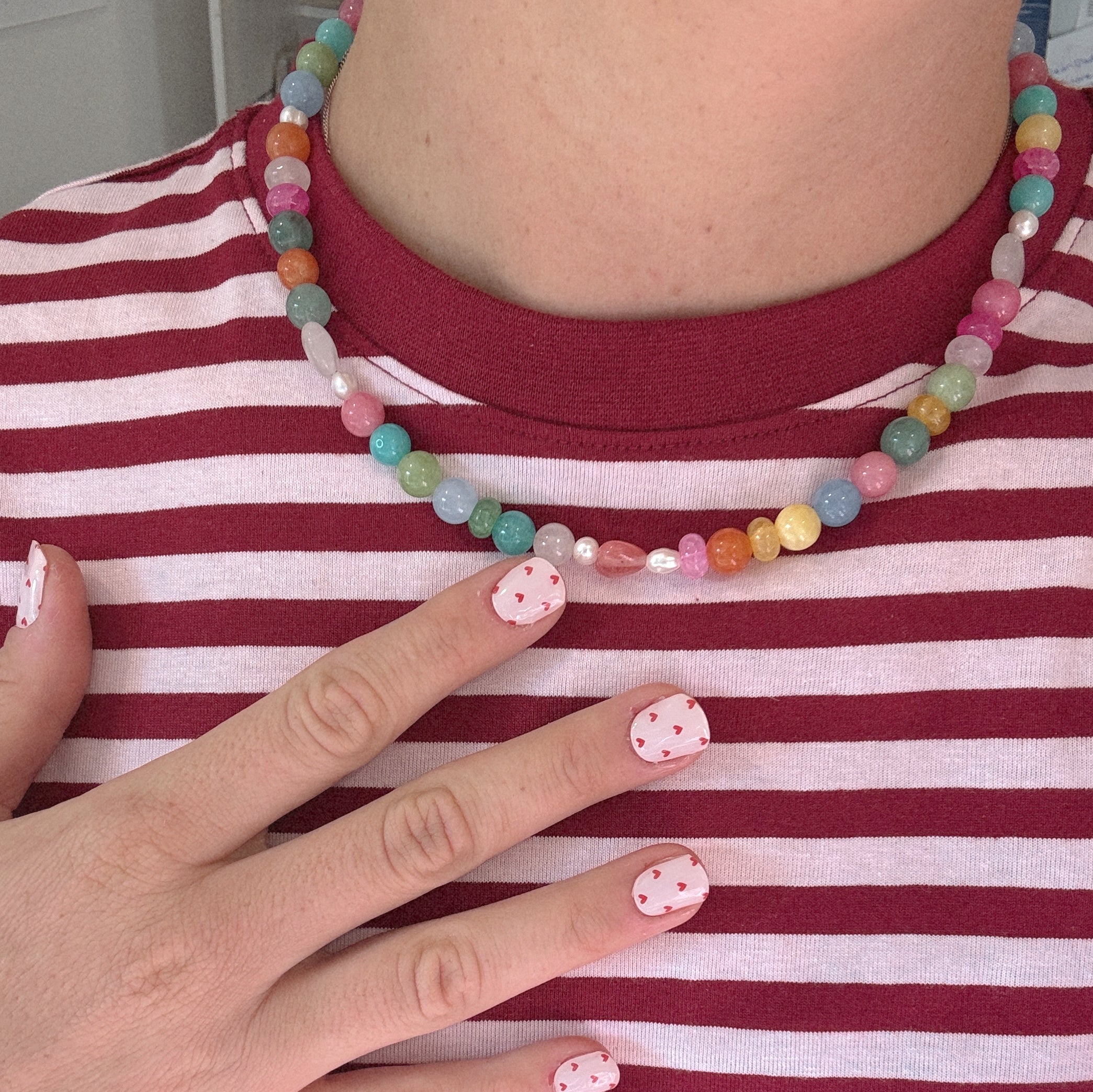 Colorful beaded necklace on a red and white striped fabric with a hand touching it.